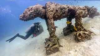 Advanced open water diver swimming by a concrete lizard structure in blue water