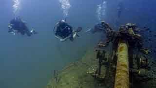 Advanced open water divers swimming by the front gun of HTMS Sattakut wreck