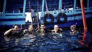 Five Open Water divers on the sea surface smiling while the boat waiting behind them