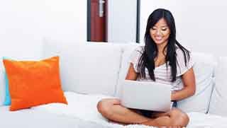 Black hair smiling women sitting home on a white sofa reading Open Water diver manual from a tablet