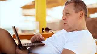 Man on a beach bed read Open Water manual from a laptop on a sunny day