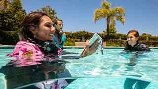 Blond women in the swimming pool reading Open Water diver manual from a tablet